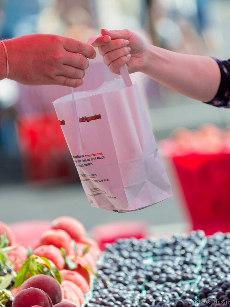 Customer receives a bag of tree-ripened Bennett Peaches at the farmers market that were picked that morning. 